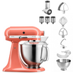 korallfarbene Kitchenaid Küchenmaschine im Set mit dem Gemüseschneider, Rührelementen, Spritzschutz und einer kleinen Schüssel auf weißem Hintergrund