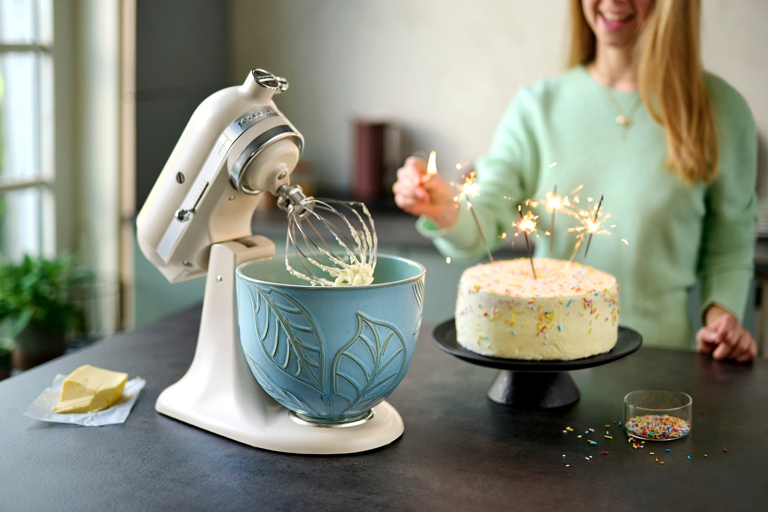 KitchenAid Küchenmaschine in creme mit blauer Schüssel mit Blattmuster neben einer Geburtstagstorte