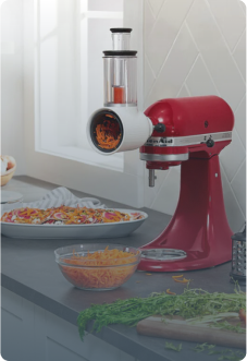 KitchenAid Küchenmaschine in rot mit angeschlossenem Gemüseschneider raspelt Möhren auf grauer Küchenplatte
