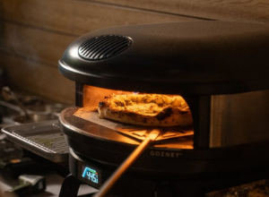 schwarzer Gozney Pizzaofen in dunkler Umgebung aus Holz mit brennender Gasflamme und einer Pizza im Ofen