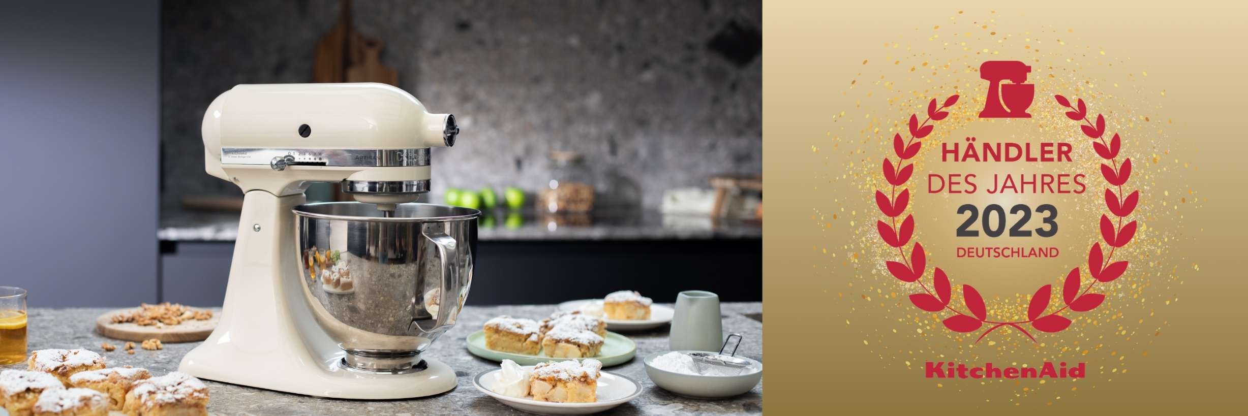 Geteilter Banner, links KitchenAid Küchenmaschine in Creme, neben mehreren Tellern Apfelkuchen, rechts das Logo KitchenAid Händler des Jahres 2023