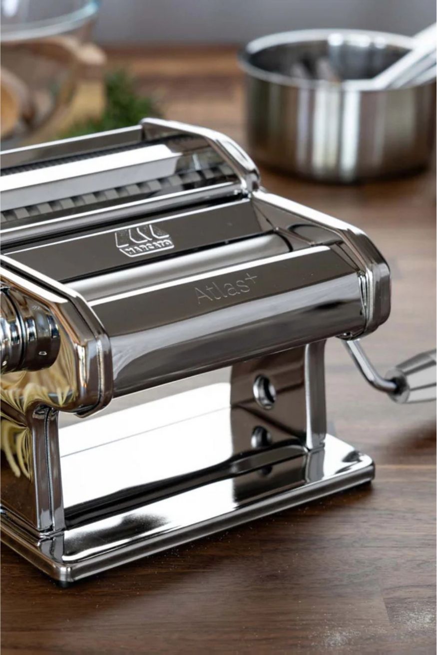 Marcato Nudelmaschine in glänzendem silber auf einer dunklen Arbeitsplatte aus Holz, im Hintergrund eine kleine Edelstahlschüssel und eine Glasschüssel