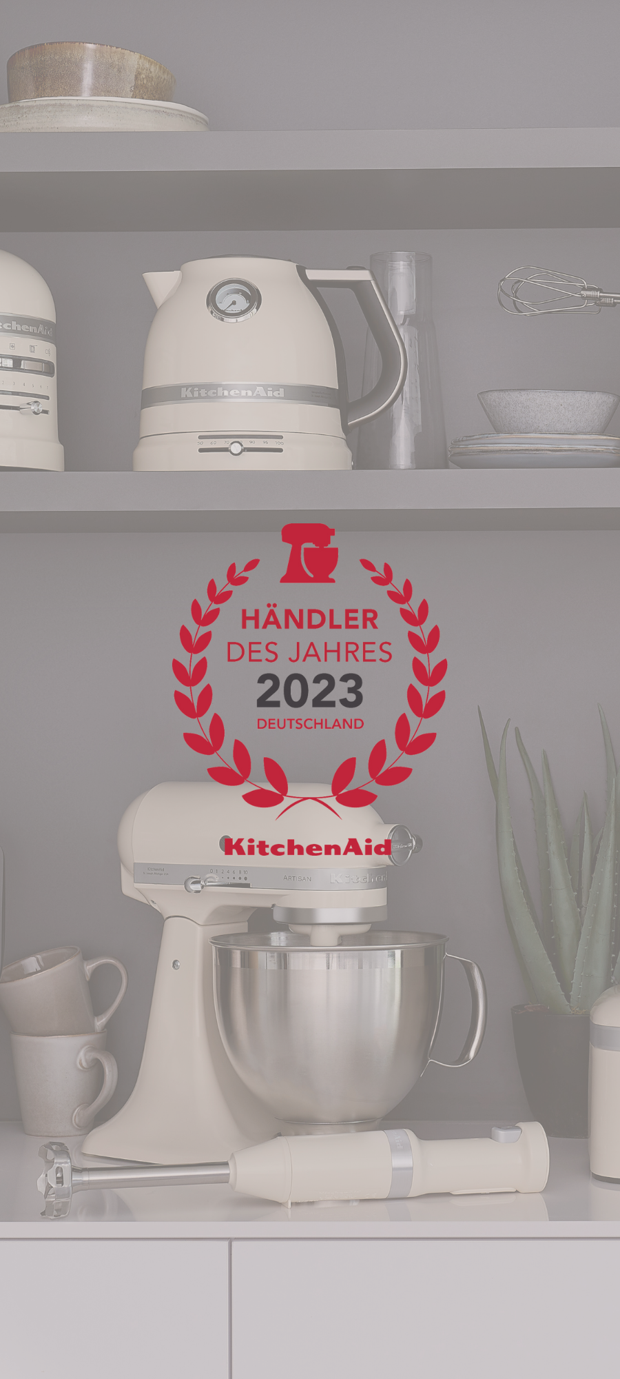 Regal mit KitchenAid Produkten im Hintergrund, im Vordergrund KitchenAid Händler des Jahres 2023 Zertifikat als Icon