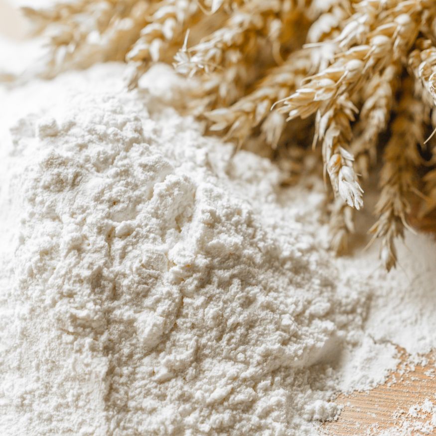 Ein Haufen Mehl neben einem Bündel Getreide auf einer Tischplatte