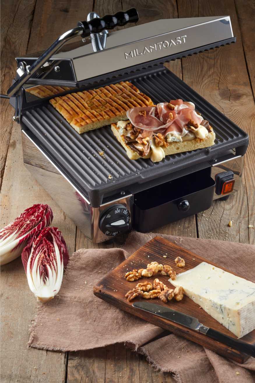 Milantoast Kontaktgrill beidseitig geriffelt auf Holzboden, darauf liegt ein Panini mit Schinken, Käse und Walnüssen