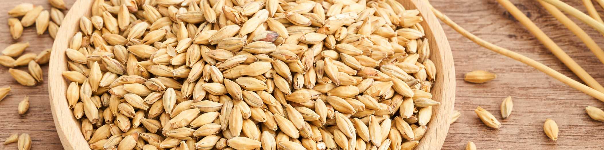 Getreidekörner in einer Holzschüssel, daneben liegen noch Getreidehalme