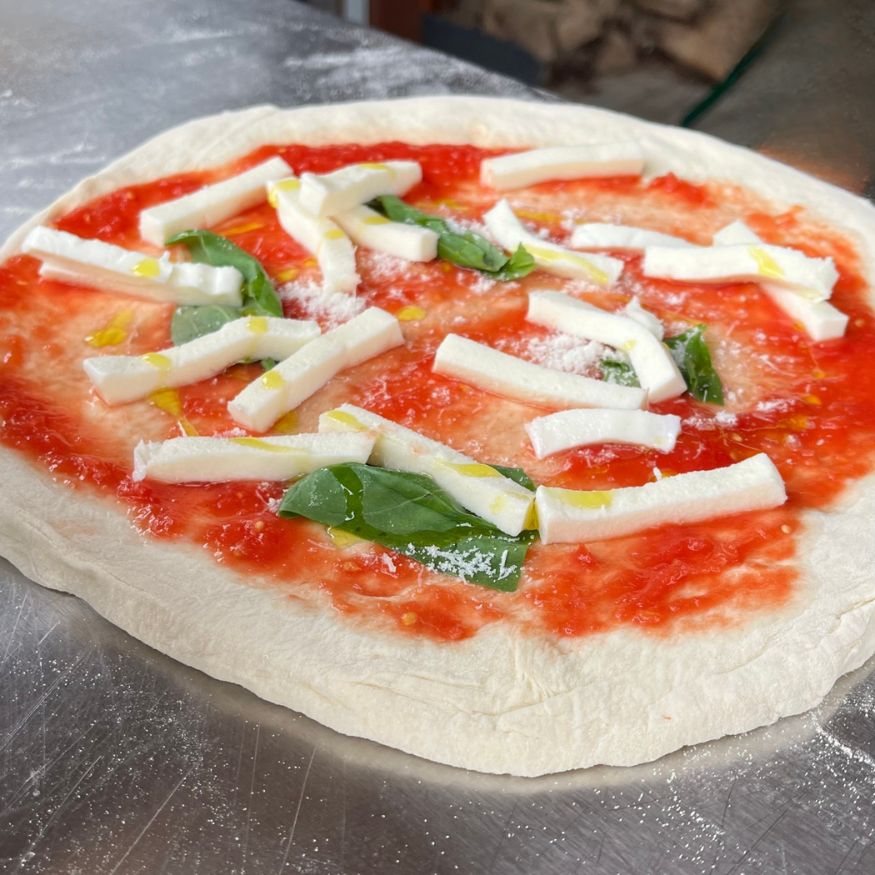 Rohe Pizza belegt mit Tomatensauce, Mozzarella, Parmesan, Basilikum und Olivenöl
