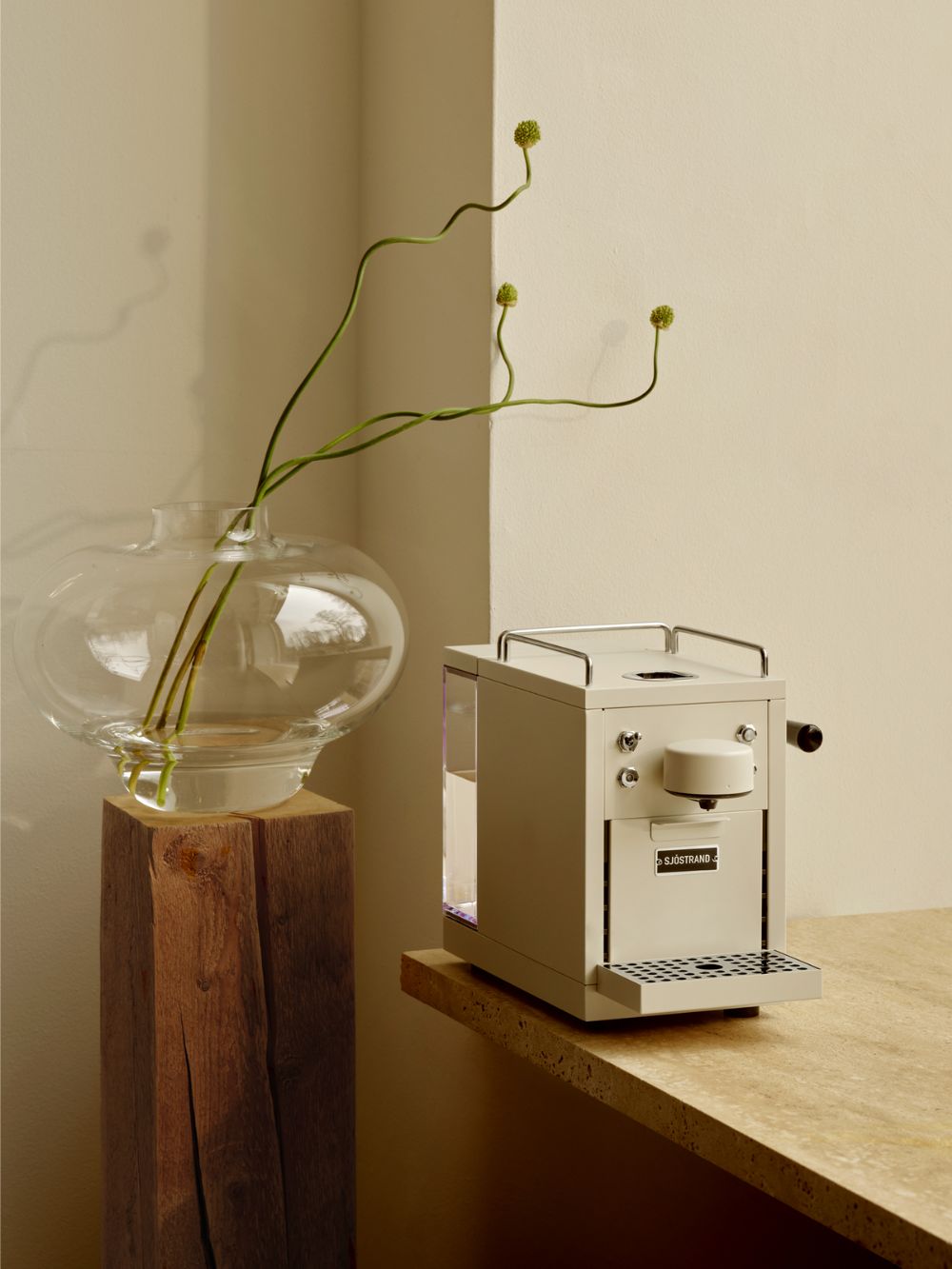 Beige Sjöstrand Kaffeemaschine steht auf einem Tisch, Bild sehr aufgeräumt, daneben eine bauchige Glasvase mit drei Blumenstängeln