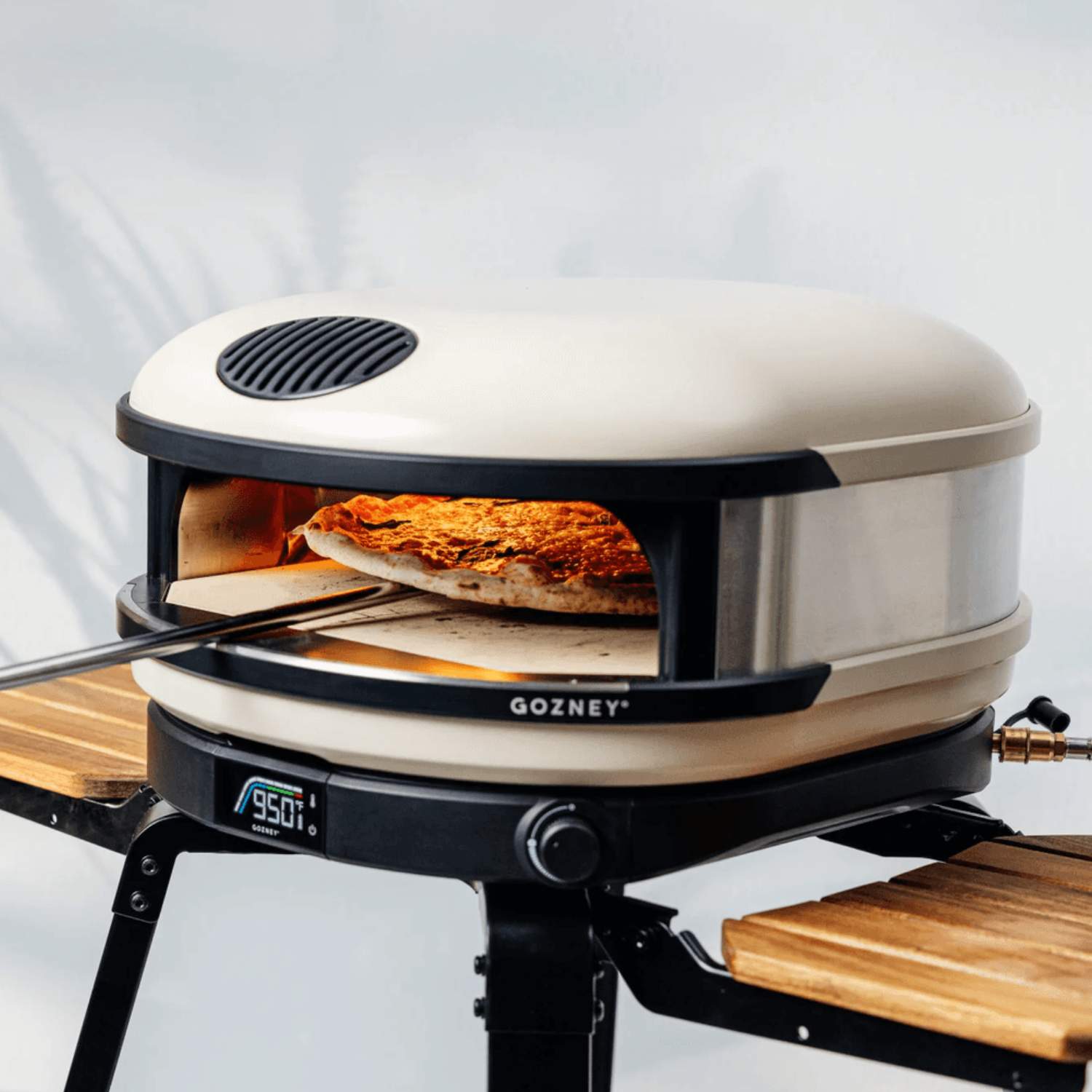 Seitliche Aufnahme des Gozney Arc XL Pizzaofens in der Farbe Créme, aus welchen grade eine frisch gebackene Pizza hervorgeholt wird.