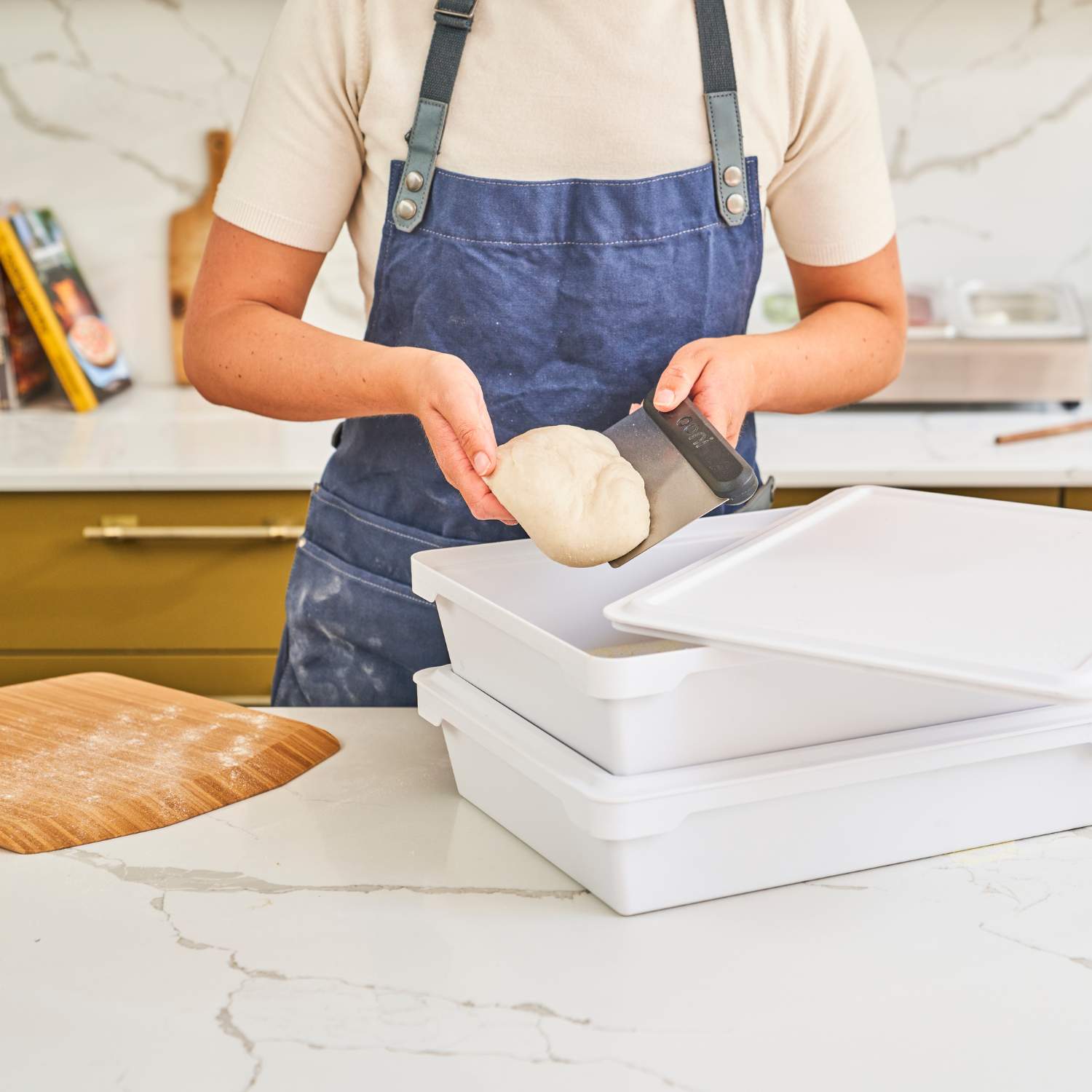 Nahaufnahme wie eine Person Teiglinge zum Pizzabacken aus einer Pizzateigbox der Marke Ooni entnommen wird. Die Person nutzt zum entnehmen einen Ooni Teigtrenner