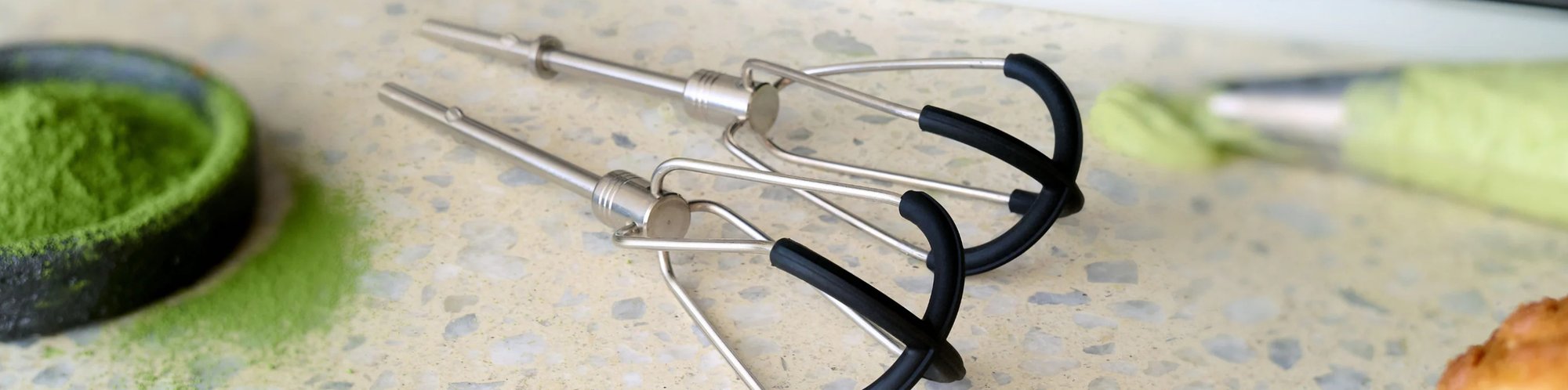 Nahaufnahme eines Rühraufsatzes für verschiedene Küchengeräte wie Handmixer oder ähnliches, welcher auf einer Arbeitsoberfläche liegt.