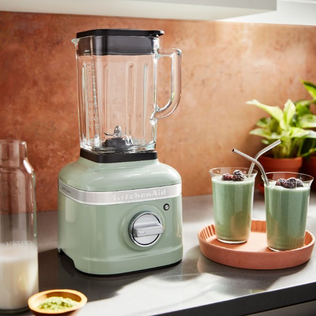 Ein KitchenAid Standmixer steht auf einem Sideboard in einer modernen Kueche. Neben dem Standmixer stehen zwei fertige Smoothies auf einem Tablett.