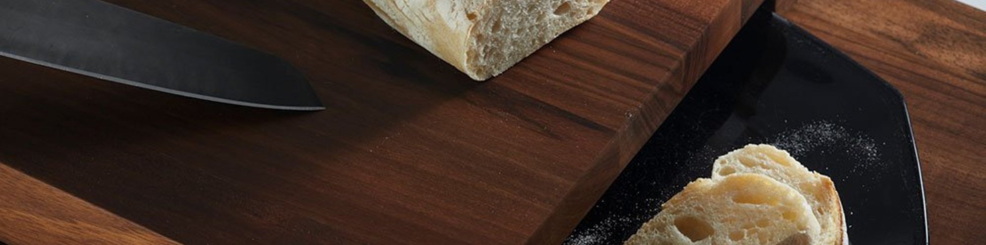 Detailaufnahme des BREKA Rustikales Servier- und Schneidebrett aus Walnuss Holz. Auf dem Schneidebrett liegen Brotabschnitte