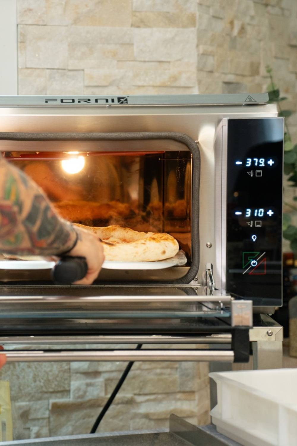 Eine frisch aufgebackene Pizza wird aus dem Forni Pizzaofen entnommen