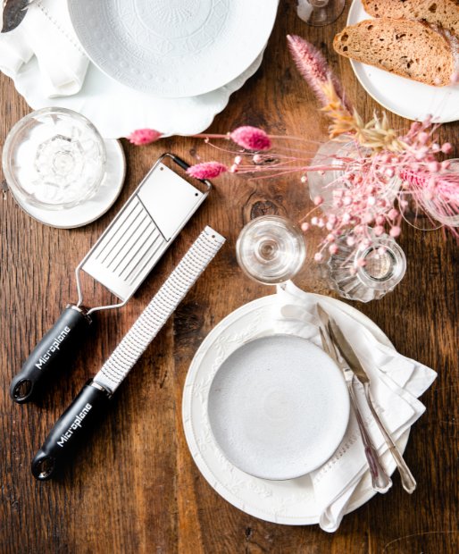 Ein rustikaler Holztisch mit verzierten Besteck, Tellern, kleinen Vasen sowie einem Miroplane Premium Zester und einem Gourmet-Slicer Hobel.