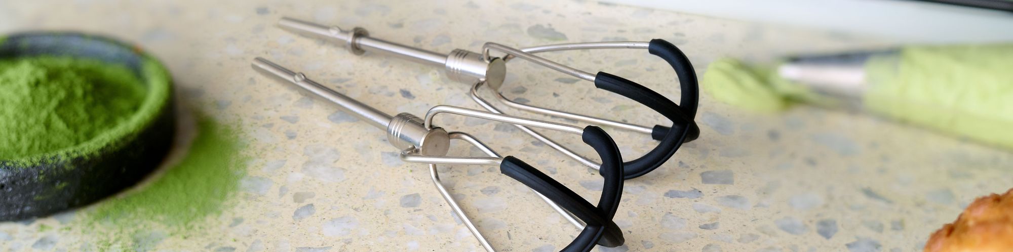 Nahaufnahme von zwei Flexi-Rührer für Handmixer (5KHMFEB2), welche mit verschiedenen Zutaten auf einem Kuechentisch aus Stein liegen