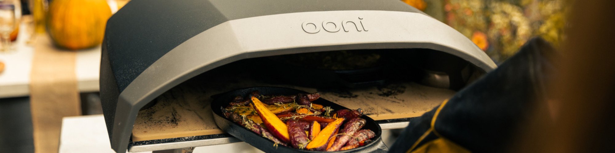 Ein Ooni Arc XL Pizzaofen aus dem Grade eine Pfanne mit gebackenen Gemüse entnommen wird.