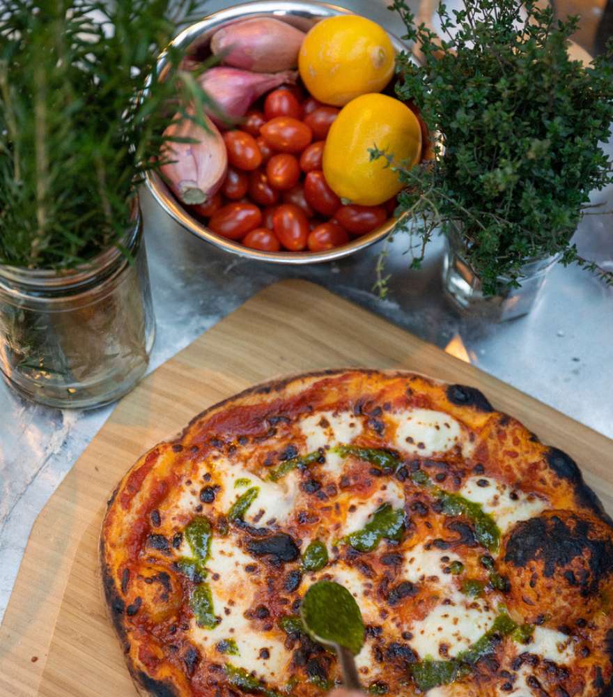 Bild einer neapolitanischen Pizza welche auf einem Holzschneidebrett liegt und neben einer Schale mit Früchten und Kräutern präsentiert wird