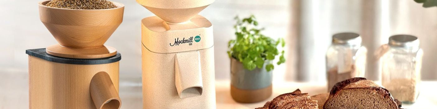 Zwei Getreidemühlen von Mockmill auf Küchentheke mit Brot und Getreidekörnern.