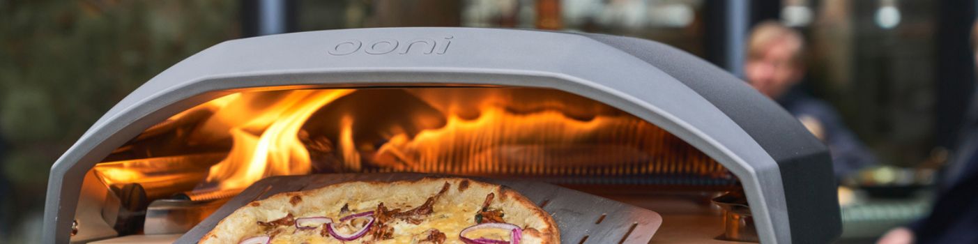 Pizza im Ooni Pizzaofen mit sichtbaren Flammen beim Backen im Außenbereich
