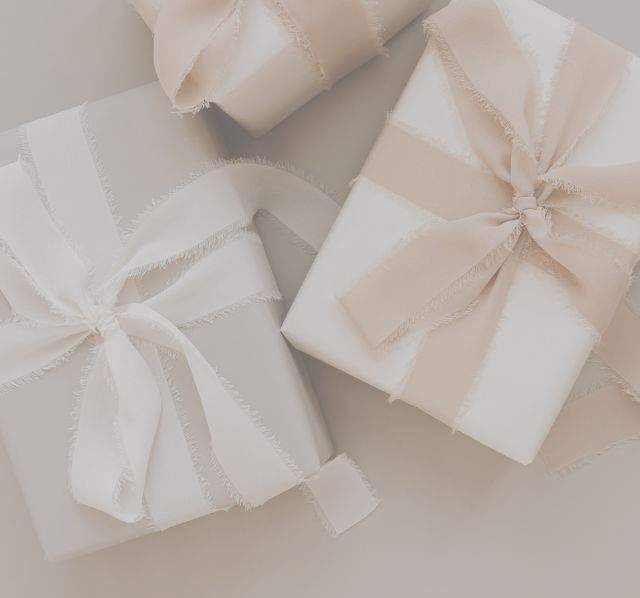 Drei Geschenke in weißen Geschenkpapier und weißen Schleifen liegen auf einem weißen Tischdecke.