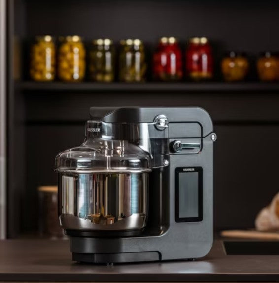 Graue Häussler Küchenmaschine im Hintergrund ein Regal mit verschiedenen eingelegten Lebensmitteln in Gläsern.