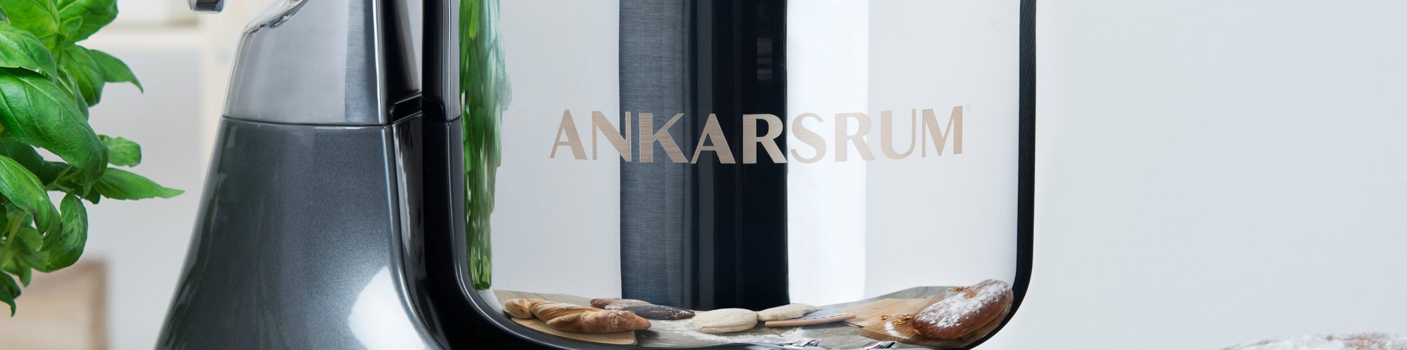 Detailaufnahme einer Ankarsrum Kuechenmaschine, in dessen Edelstahlschuessel sich verschiedene Backwaren spiegeln