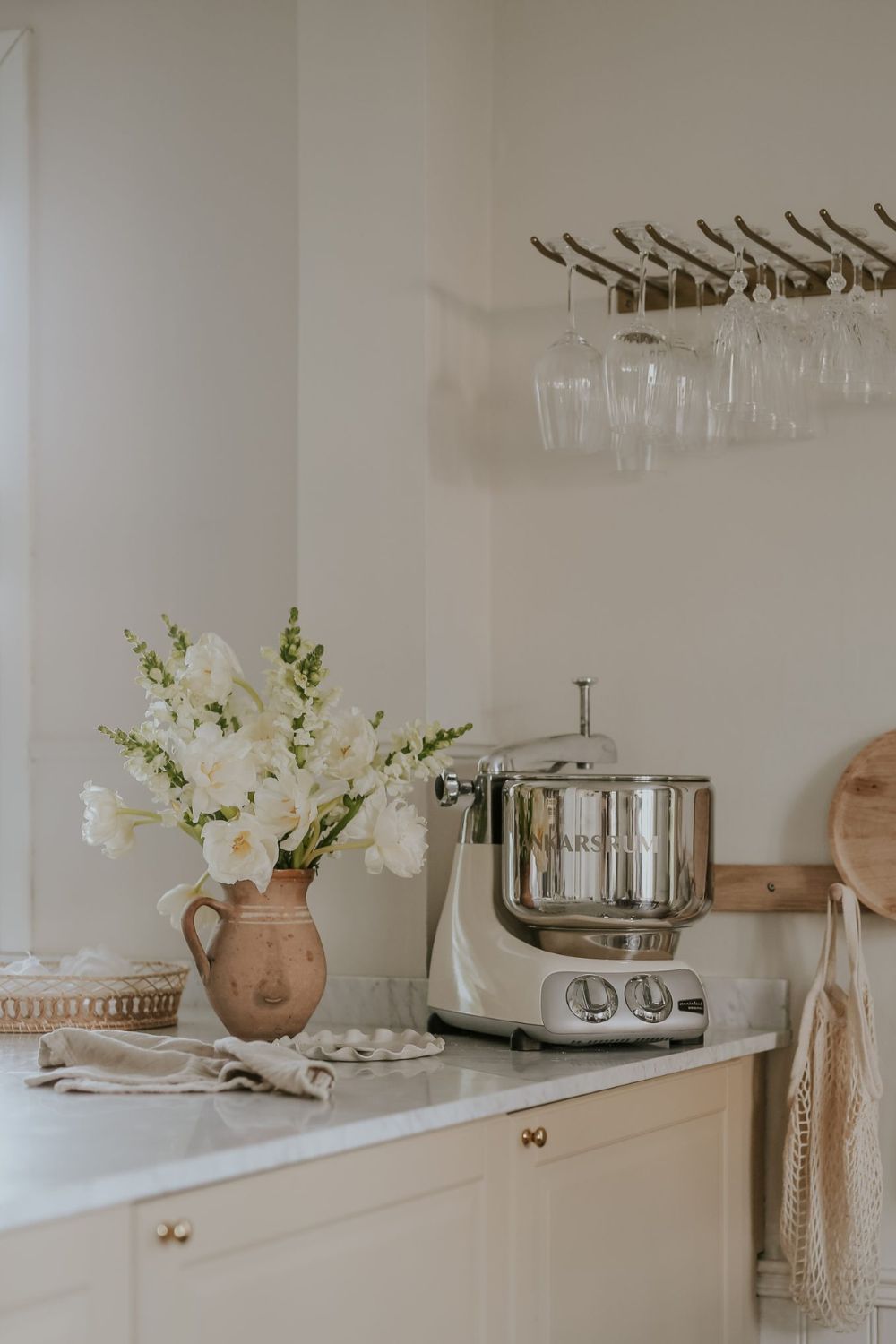 Eine Ankarsrum Kuechenmaschine steht auf einem Kuechenschrank, zusammen mit eine Blumenvase, Gläsern und einem Brotkorb.