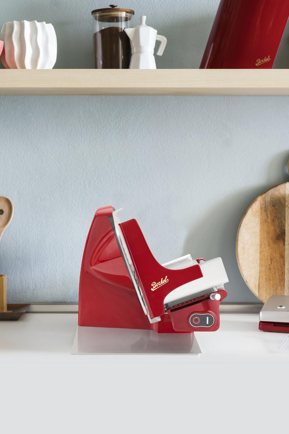 Eine Berkel Brot- und Aufschnittmaschine Home Line 200 Plus in der Farbe Rot steht auf einer Glasplatte zwischen verschiedenen Kuechengegenständen