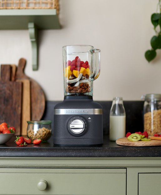 Ein KitchenAid K400 Standmixer Artisan in der Farbe Onyx Schwarz steht auf einer modernen Kueche auf einer Arbeitsplatte.  In dem Standmixer befinden sich verschiedene Obst- und Nusssorten.