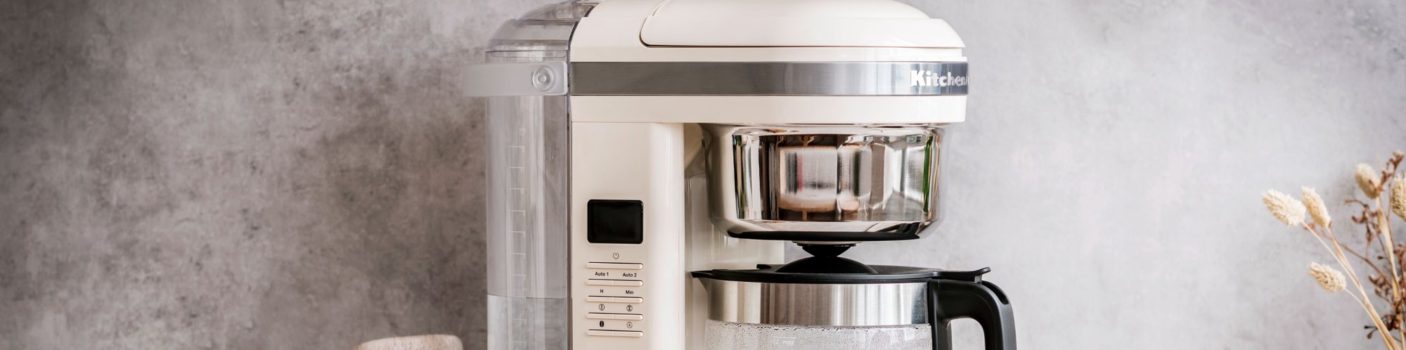 KitchenAid Kaffeemaschine 5KCM1209E KitchenAid in der Farbe Crème vor einer grauen Wand