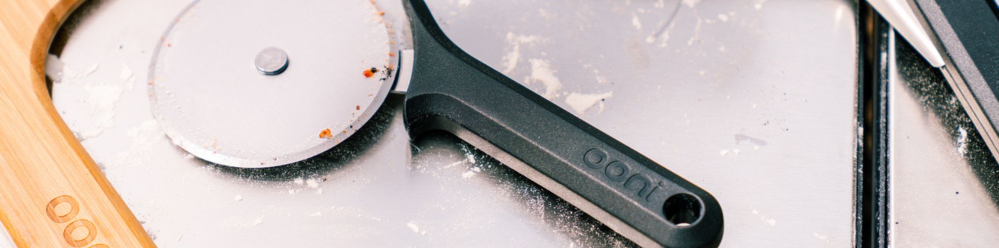 Detailaufnahme eines Ooni Pizzaschneider wie er auf einem Bambus Pizzabrett liegt