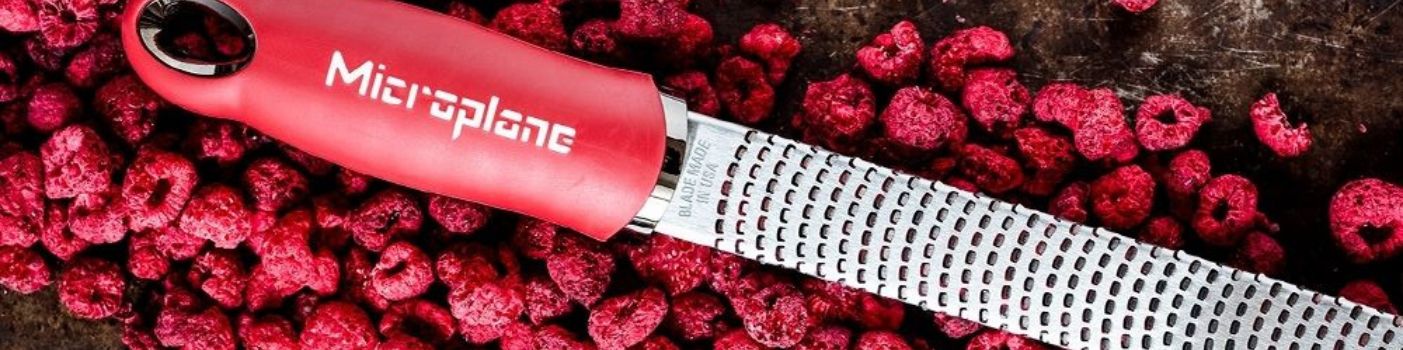 Microplane Reibe mit rotem Griff liegt auf Himbeeren.