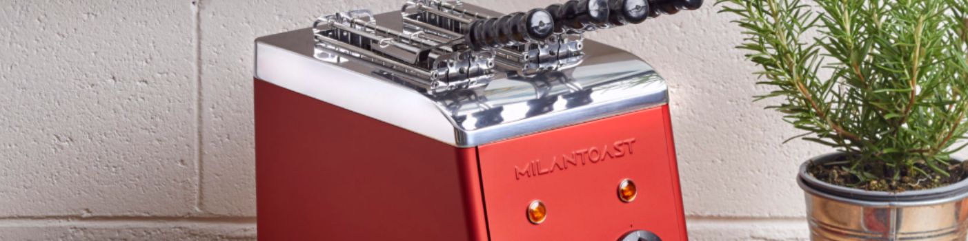 Roter Milantoast Toaster mit Metallaufsatz auf Küchenarbeitsplatte neben Topfpflanze.