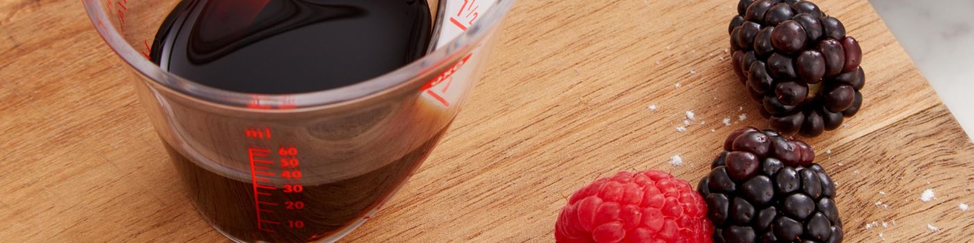 Oxo Messbecher mit dunkler Flüssigkeit und Beeren auf Holzbrett in Küche.