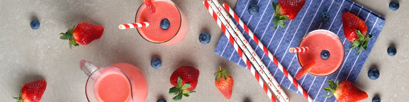 Gläser mit Erdbeer-Smoothie, Strohhalme und frische Beeren auf Tisch verteilt.