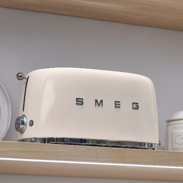 Ein Smeg Toaster in der Farbe Creme steht auf einem Holzregal in einer Kueche.