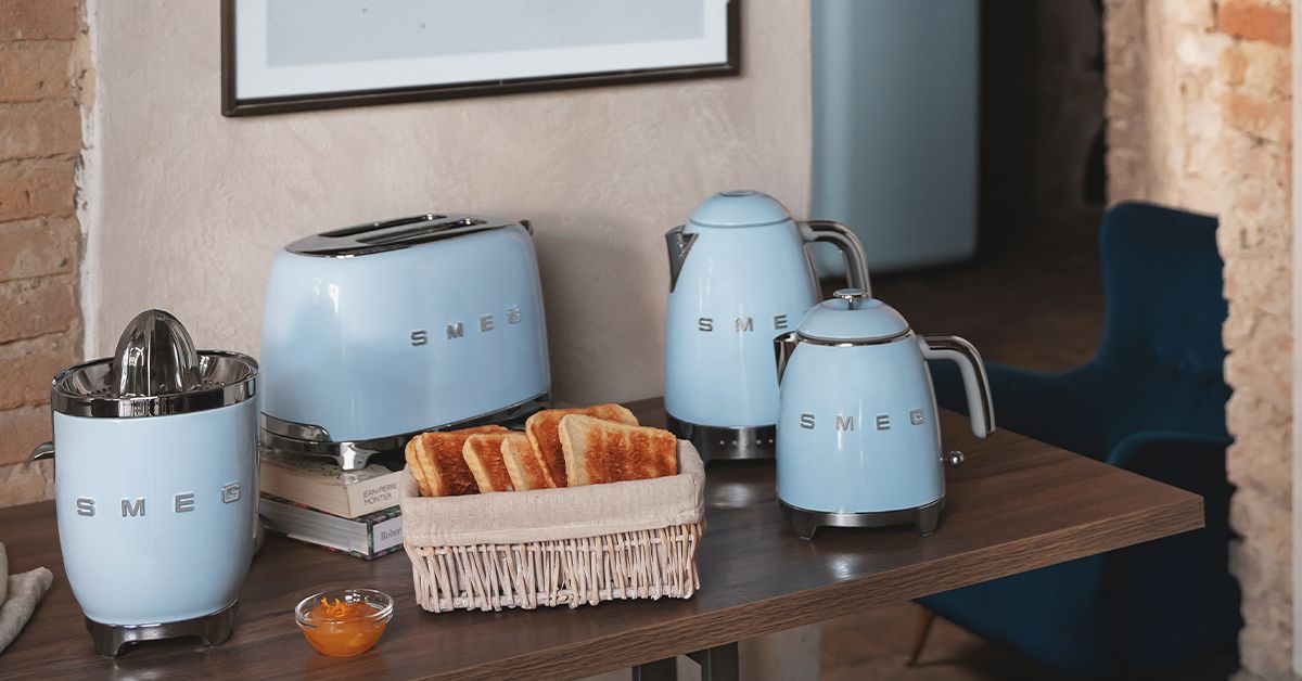 Ein Kuechentisch in einem Wohnzimmer auf dem verschiedene Kuechengeraete der Marke Smeg stehen.