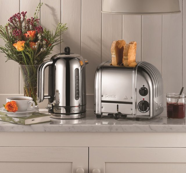 Kuechenzeile mit Marmor Arbeitsplatte auf der ein Dualit Classic 2-er Toaster in der Farbe Silber steht. Neben dem Toaster steht ein Dualit Wasserkocher sowie ein Buch mit einer Tasse Tee darauf und eine Blumenvase.